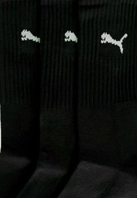 Schwarze Sportsohlen mit gerippten Bündchen und einem kleinen grauen Puma-Logo auf der Vorderseite. Glatte Textur und Design in Knöchellänge.