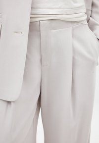 Heledhall hall suit tekstuuriga kangast, millel on pleediga püksid ja kitsas jakk. Jakil on nähtavad õmblused.