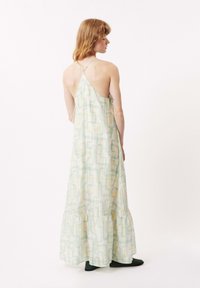 Robe maxi en tissu vert clair avec des motifs géométriques abstraits. Les bretelles spaghetti et l'ourlet en niveaux ajoutent de la texture et de l'intérêt visuel.