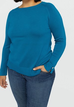 Teal langmouwtrui met geribbelde zoom en manchetten, met een ronde halslijn en een aangesloten pasvorm. Dragen met blauwe jeans.