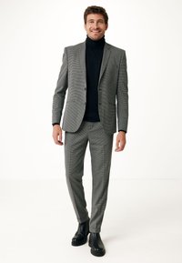 Completo a scacchi grigio con una vestibilità su misura, abbinato a un maglione a collo alto nero e stivali neri con suola spessa. Tessuto liscio e design strutturato.