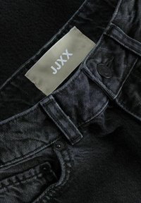 Jeans de mezclilla negros con un acabado texturizado, que presentan una etiqueta visible etiquetada como "JJXX" y un cierre con un botón redondeado negro.