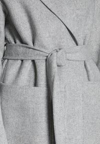 Accappatoio grigio in lana con design avvolgente, cintura annodata e due tasche frontali. Tessuto strutturato con un aspetto morbido e peloso.