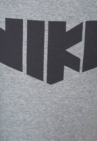 Šedé bavlněné tričko s výrazným černým blokovým písmenkovým logem "NIKI" na hrudi, s hladkou texturou a volným designem.