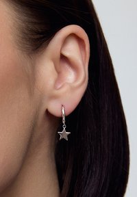 Srebrna kolczyki w kształcie koła z wiszącą zawieszką w kształcie gwiazdy. Gwiazda ma gładką powierzchnię, a obręcz ma wypolerowane wykończenie, co potęguje jej blask.