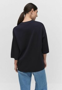 Marineblauwe oversized trui met mouwen tot de elleboog, gemaakt van zachte stof. Heeft een ronde halslijn en een relaxte pasvorm, gecombineerd met lichte jeans.