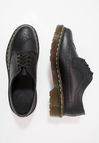 Chaussures noires en cuir avec des détails en brogue, bout rond, design à lacets et surpiqûres jaunes. Semelles en plateforme translucides avec texture striée.