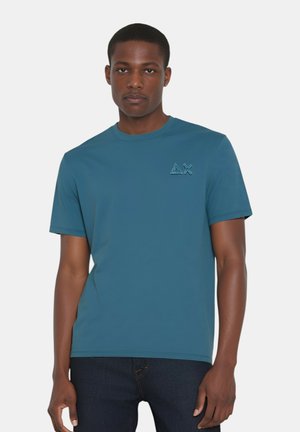 T-shirt corto a maniche corte di colore teal con scollatura a girocollo, caratterizzato da un logo testurizzato sul lato sinistro del petto e un design liscio, leggermente aderente.