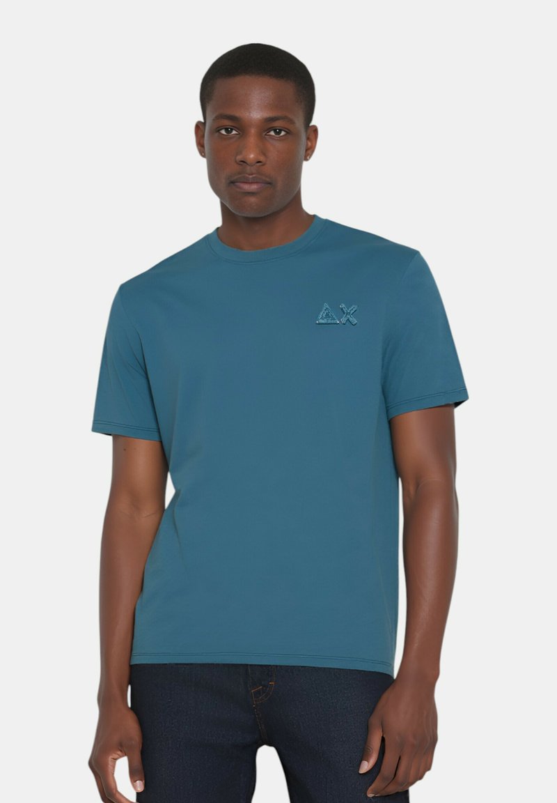T-shirt a maniche corte color turchese, realizzata in tessuto liscio, con una discreta patch logo sul petto a sinistra. Design classico con collo rotondo.