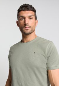 Lichtgroen T-shirt met korte mouwen en een ronde halslijn, gemaakt van zachte stof, met een klein zwart logo op de borst.