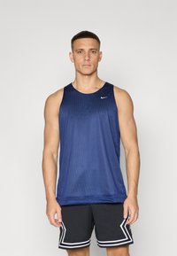 Mørkeblå treningstopp i atletisk stil med pustende mesh-struktur, rund halslinning og liten hvit logo. Kombinert med svarte shorts med hvite detaljer.