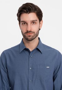 Camicia button-up blu da uomo realizzata in tessuto testurizzato; presenta una tasca sul petto e un'etichetta del marchio sulla tasca, con un classico design del colletto.
