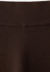 Tissu tricoté brun foncé avec une ceinture côtelée et une couture visible courant verticalement au centre.