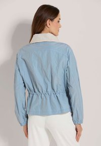 Lichtblauwe jas met een aangesnoerde taille, elastische manchetten en een contrasterende crèmekleurige kraag. Glad materiaal, lichtgewicht stof en een eenvoudig ontwerp.