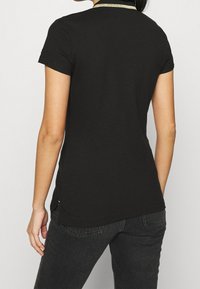 Sort kortærmet T-shirt med en rund halsudskæring og en gylden detalje ved kraven. Stoffet er glat og let tætsiddende ved taljen.