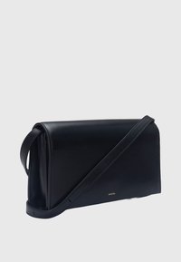 Sac à bandoulière en cuir noir avec une longue sangle, de forme rectangulaire, et petit logo doré "VINCE." à l'avant.