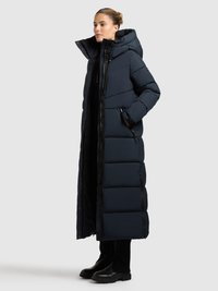 Sötétkék, hosszan érő, steppelt tengerész dzseki nagy kapucnival és cipzáras zsebekkel. Fekete ruházatra és fekete csizmára hordva.