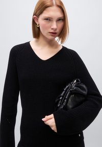 Pull noir en maille avec col en V et manches longues larges. Associé à une pochette noire froncée. Texture lisse, détails minimaux.