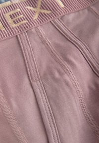 Boxers seamless en mauve clair avec une ceinture élastique côtelée, ornés de lettres dorées et de coutures à plat. Tissu doux et extensible.
