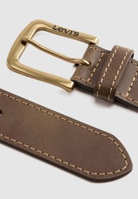 Cinturón de cuero marrón con hebilla de latón, con costura contrastante. La hebilla está grabada con "Levi's." Los extremos están cortados rectos y lisos.