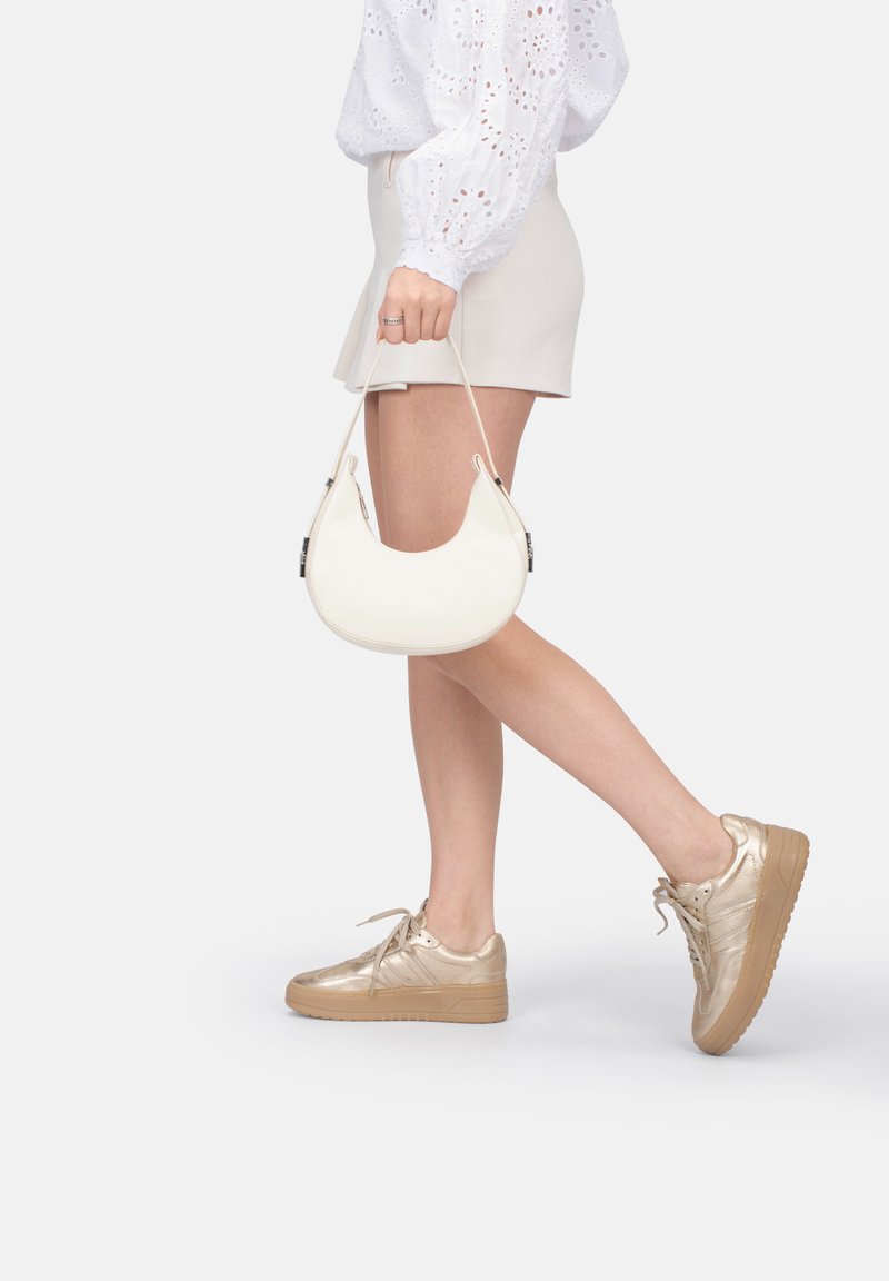 Borsa bianca con una forma curvada e un sottile manico, abbinata a una gonna beige e sneakers metallici oro con suola spessa.