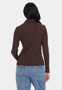 Rjava rebrasta dolgosleeve majica s ovratnikom, ki ima prilegajoč dizajn. V kombinaciji z svetlo modrimi kavbojkami visoke pasu.
