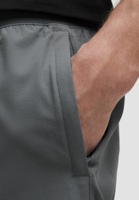 Un gros plan d'une main reposant dans la poche d'un short de sport gris, mettant en valeur la texture du tissu et une position détendue.