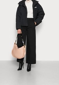 Svart pufferjacka, höghalseribbad vit topp, svarta vida byxor, svarta klackar, håller en läderväska i puderrosa med svarta remmar.