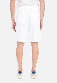 Pantaloni corti bianchi in lino con una vestibilità rilassata, caratterizzati da una texture liscia e una cintura elastica. Abbinati a sneakers di colore chiaro.