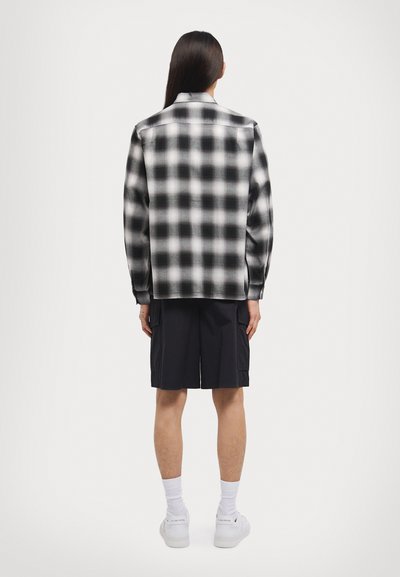 Black and white plaid flannel shirt with a relaxed fit, long sleeves, and button details, paired with dark shorts and white sneakers.