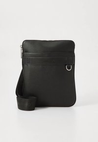 Mala de tiracolo preta texturizada com fecho de correr, alça de tecido ajustável e pequeno detalhe em anel de metal na frente.