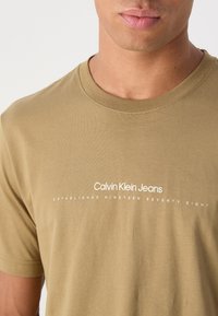 Olive green short-sleeve t-shirt made of soft cotton. Features white text: "Calvin Klein Jeans" and "ESTABLISHED NINETEEN SEVENTY EIGHT."