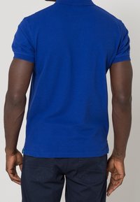 Blå kortärmad pikétröja med klassisk krage, tillverkad av bomull, med rak fåll och en jämn yta. Inga synliga mönster.