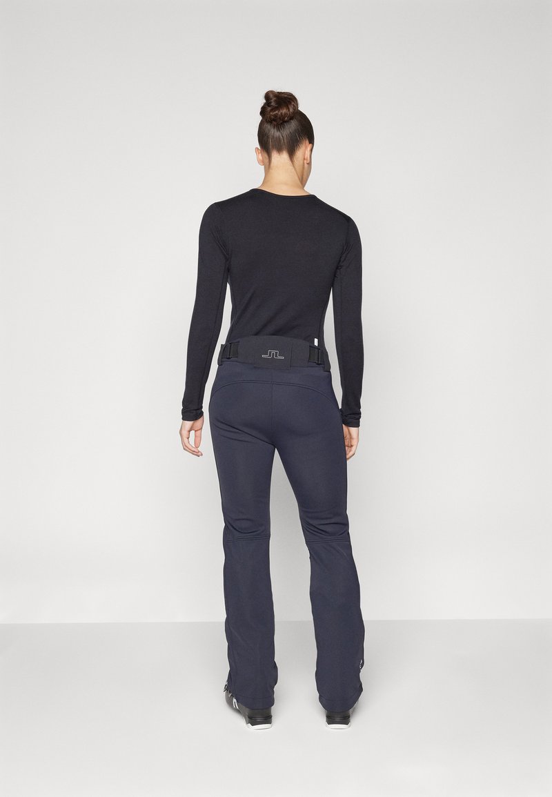 Schwarzes Langarmoberteil mit figurnahen Design, kombiniert mit dunkelblauen Skihosen mit einem Gürtelbund und ausgestellten Beinen. Glatte Textur, geeignet für den Winter.