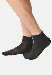 Harmaat nilkkasukat, valmistettu pehmeästä, hieman läpikuultavasta materiaalista, joissa on resorireunus ja vartalonmyötäinen muoto.