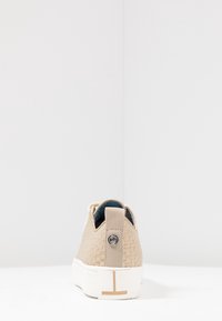 Beige pletené tenisky s texturovaným svrškem, bílou gumovou podrážkou a zadním uchycením. Mají logo na zadní straně a kontrastní interiér.