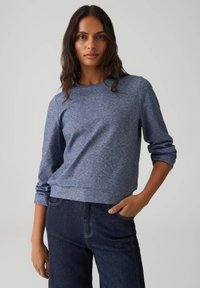 Blauwe gemêleerde sweatshirt met een ronde hals, lange mouwen en een losse pasvorm, gecombineerd met donkere spijkerbroek. Gladde textuur en casual ontwerp.