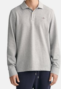 Man wearing light grey long-sleeve polo shirt with collar and buttons paired with dark navy pants.