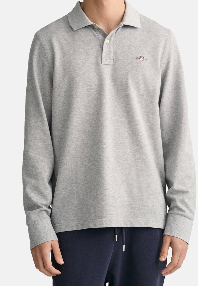 Man wearing light grey long-sleeve polo shirt with collar and buttons paired with dark navy pants.