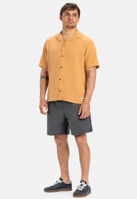 Short-sleeve, collared shirt in light orange linen, paired with dark gray shorts. Casual sneakers complete the outfit.
