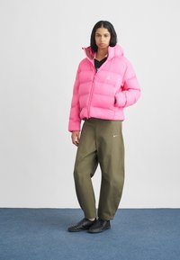 Chaqueta puff rosa con cremallera frontal, acolchado en forma de rombo y capucha. Combinada con pantalones sueltos de color verde oliva y zapatillas negras.