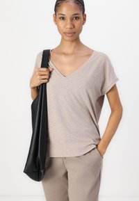 Beige T-shirt med V-hals, korta ärmar och mjuk textur. Kombinerad med beiga byxor och en svart axelväska. Minimalistisk design.