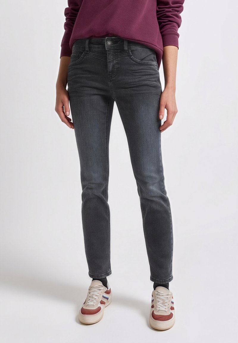 Šedé úzké džíny z denimu se středně vysokým pasem, pěti kapsami a jemným vyblednutím, doplněné béžovo-červenými teniskami.