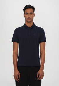Navy blue polo shirt made of cotton, featuring a classic collar, short sleeves, and a subtle EA7 logo on the left chest area.
