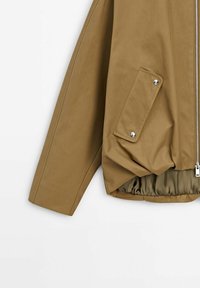 Veste kaki avec une fermeture éclair à l'avant, poche latérale avec fermeture à pression, bas élastiqué et texture lisse et mate.