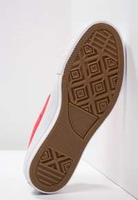 Red canvas sneaker with a white rubber sole and brown textured tread. Features diamond pattern and branding on the sole.