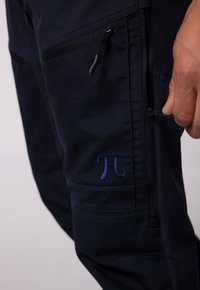 Námořnické látkové kalhoty s kapsou na zip a vyšitým logem π v modré barvě. Design zahrnuje více kapes a strukturovaný povrch.