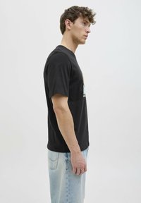 Camiseta negra de manga corta con un estampado gráfico en el frente, combinada con jeans de color azul claro, presentada sobre un fondo blanco liso.