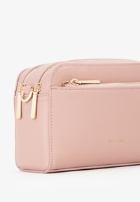 Różowa kosmetyczka o teksturowanej powierzchni z podwójnymi suwakami, złotymi akcentami i gładkim wykończeniem. Posiada przednią kieszeń do dodatkowego przechowywania.