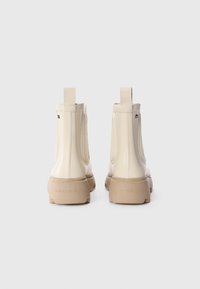 Bottines couleur crème avec une finition brillante, dotées de panneaux élastiques sur les côtés, de tirants et de semelles en caoutchouc beige. Détails du logo sur le talon.